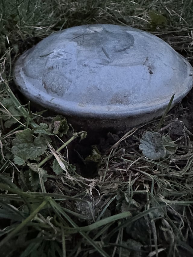 r/whatisthisthing - I recently bought a new house and this is in my backyard. Looks like a cap of some sort, about 6 inches in diameter. Feels like metal and is embedded into the ground.