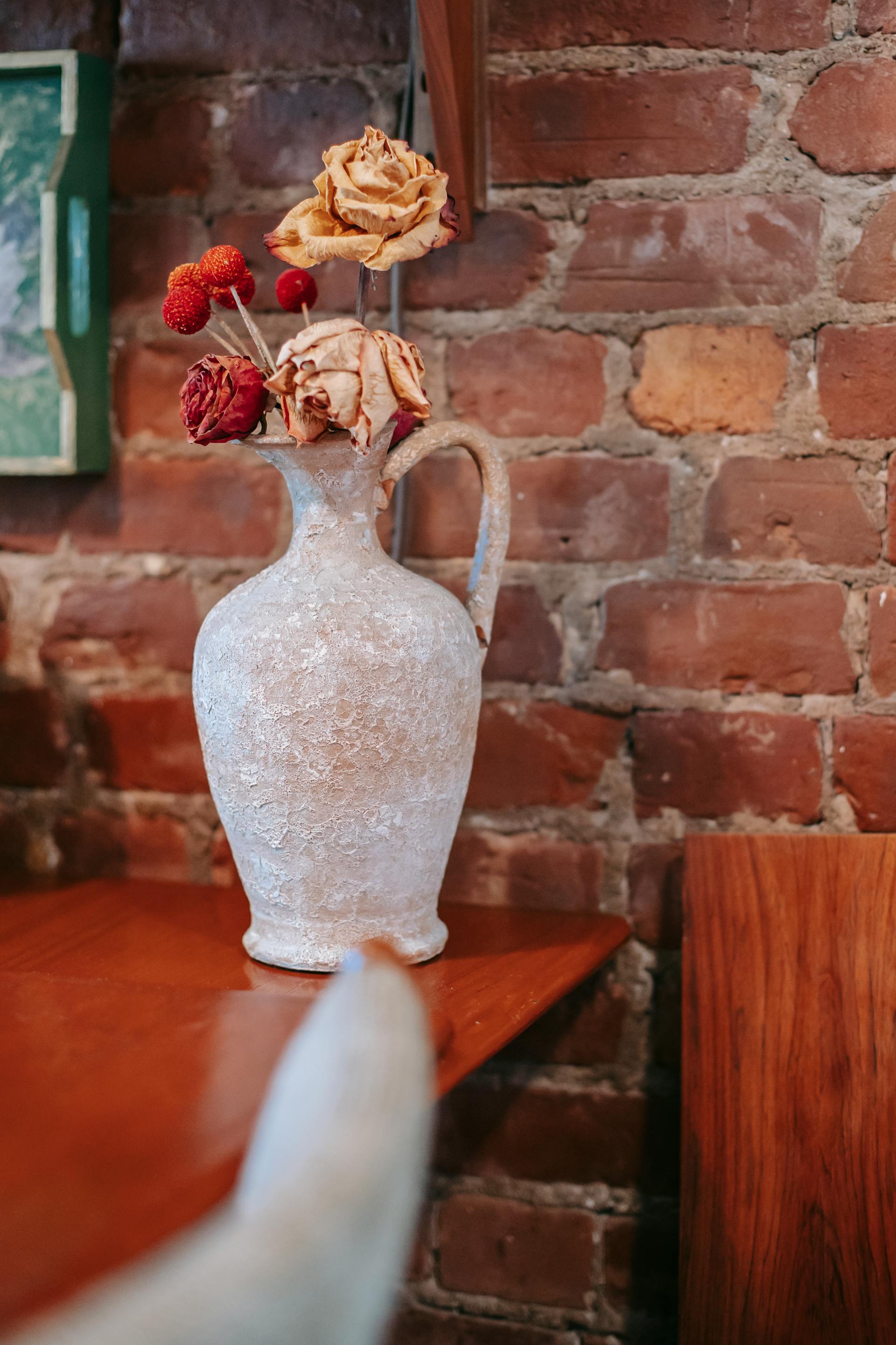 A vase with dried roses on a wooden table | Source: Pexels